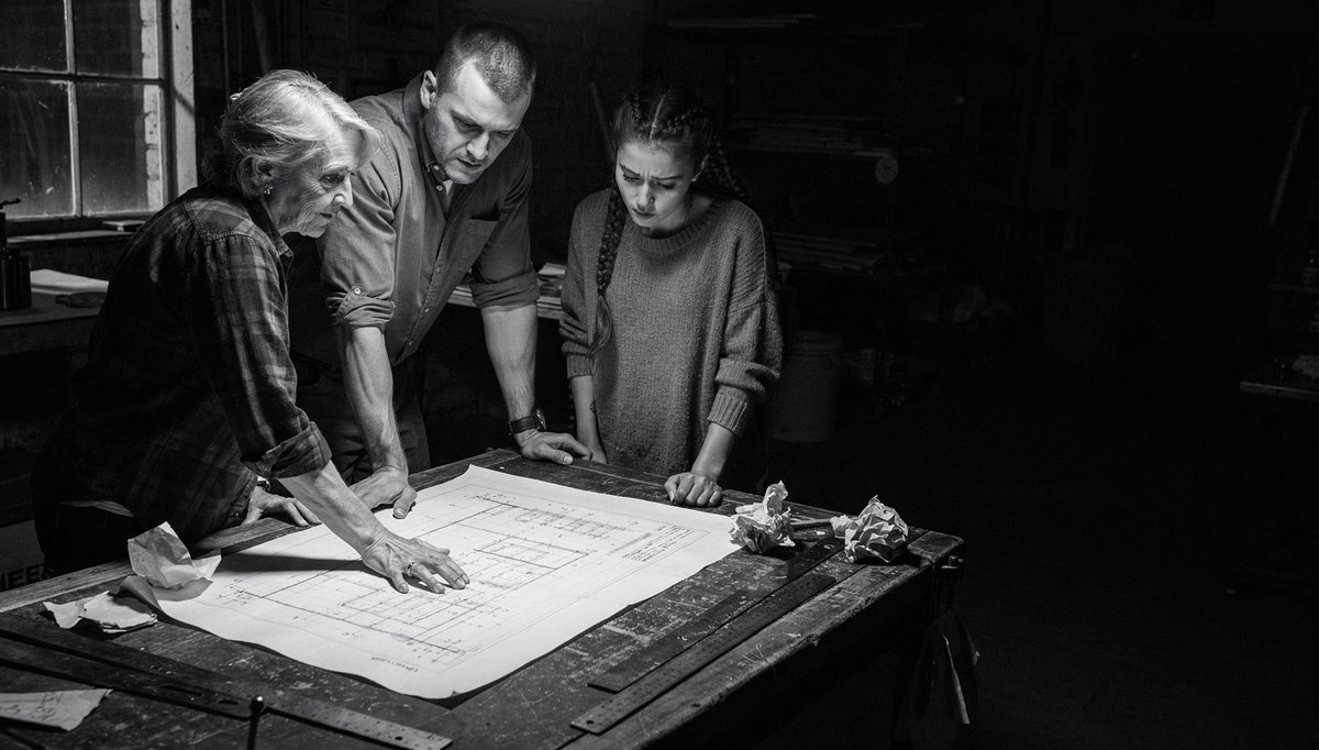 Three workers collaborating over blueprints showing team synergy